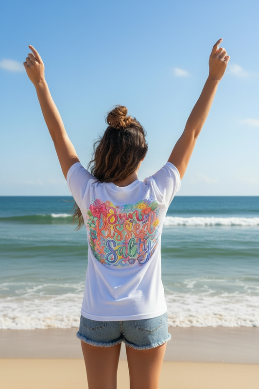 Woman on beach with arms raised showing back of Sun Kissed & Salty white t-shirt